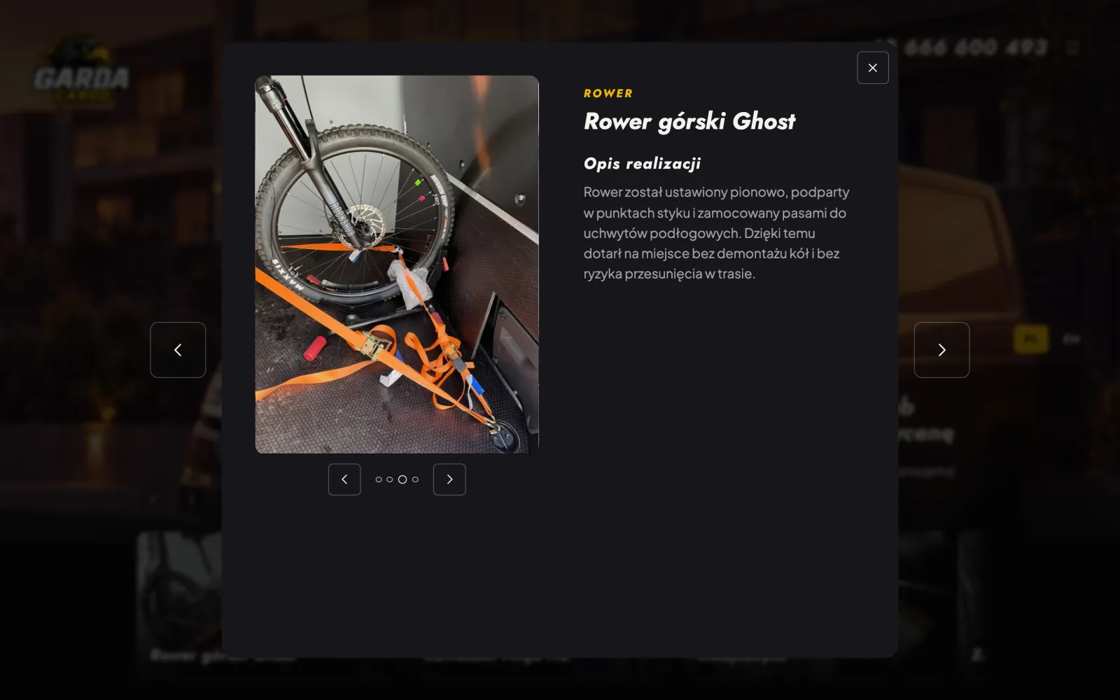 Otwarty panel realizacji „Rower górski Ghost”: zdjęcie roweru zamocowanego pomarańczowymi pasami w busie, galeria ze strzałkami i opis realizacji.