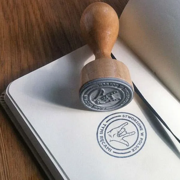 Wooden rubber stamp and its inked Polisze mark pressed into a notebook.