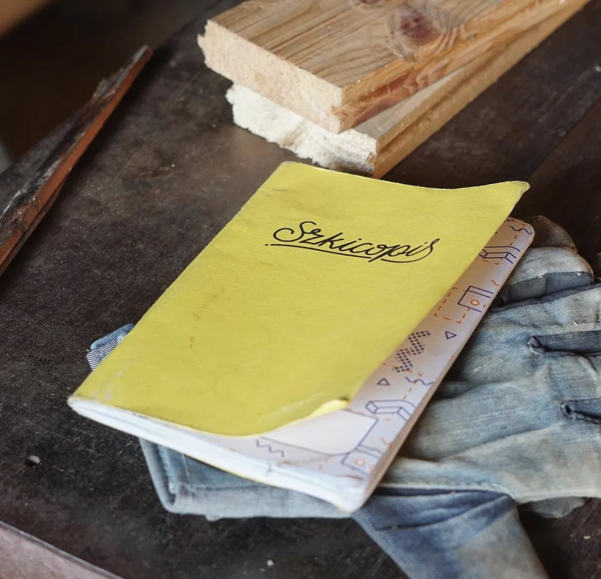 A yellow Szkicopis notebook resting on a worn workbench next to a block of wood.