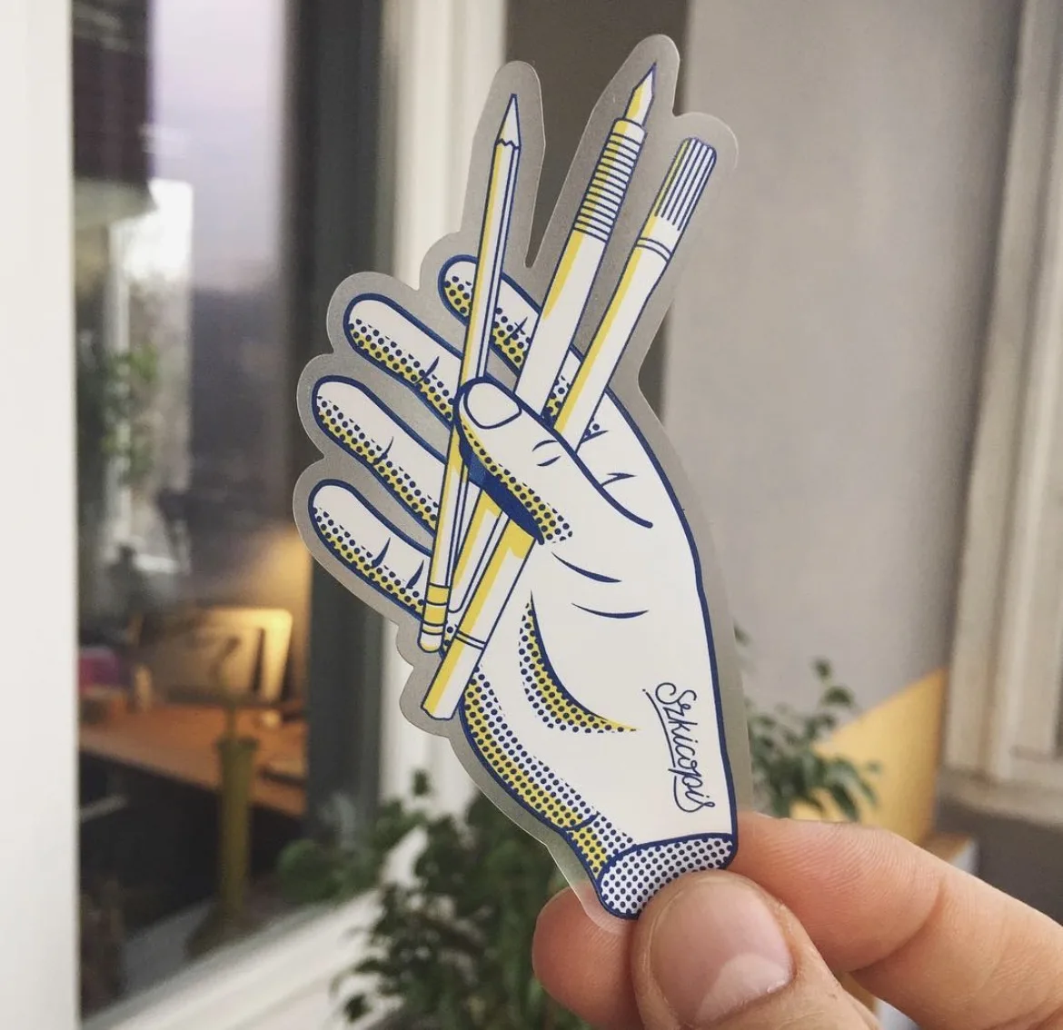 The Szkicopis hand die-cut sticker, held up in front of a window.